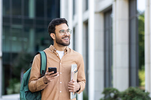 istock Young man walking through the city with a backpack, student smiling outside university campus in casual clothes 2207319208