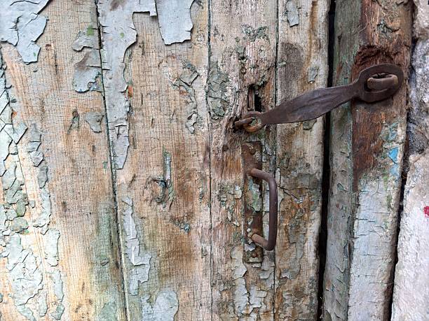 Horizontal closeup photo of part of an old worn white painted wooden door and decorative rusty lock on the front facade of a house on the street, La Rochelle, France.