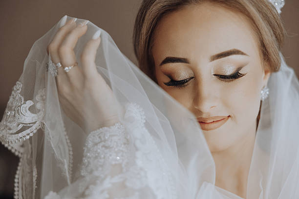 A woman is wearing a white veil and a ring on her finger. She is looking at the camera with a smile on her face