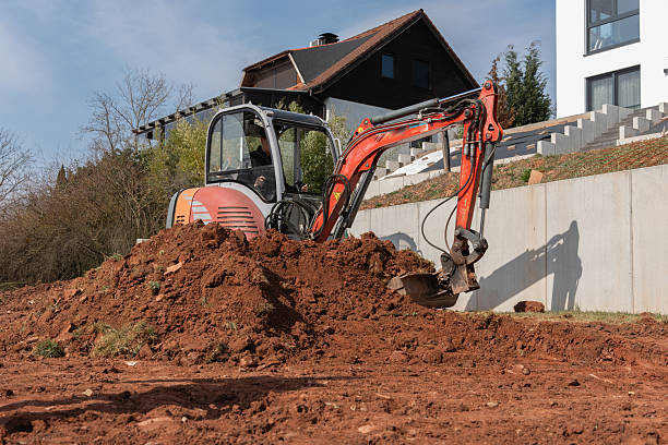 istock A compact excavator removes soil on a sloped plot near a modern residential building. The construction site is prepared for landscaping or foundation work. 2207320255