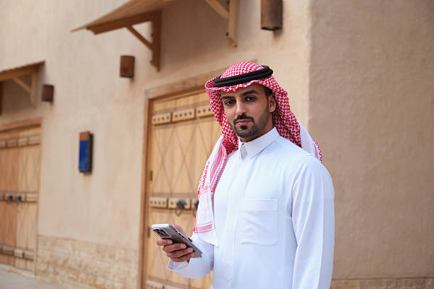 istock Man Wearing Traditional Attire Using Smartphone in a Historic Market Setting 2207321520