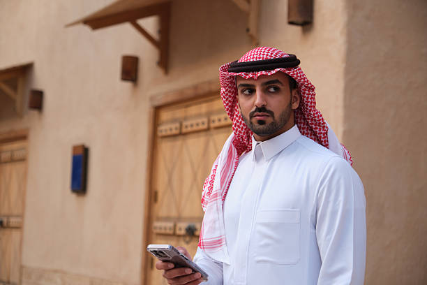 istock Man Wearing Traditional Attire Using Smartphone in a Historic Market Setting 2207321553