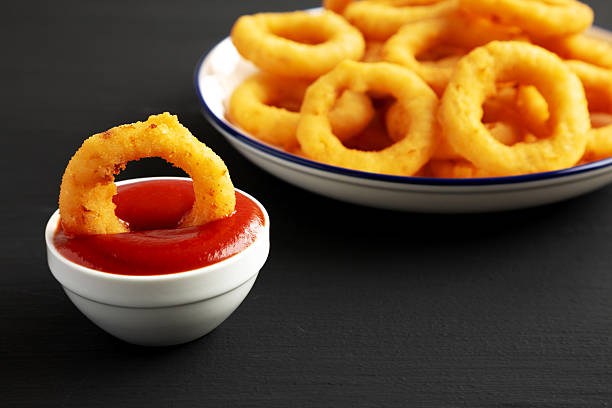 Homemade Breaded Onion Rings with Ketchup on a Plate on a black background, side view.
