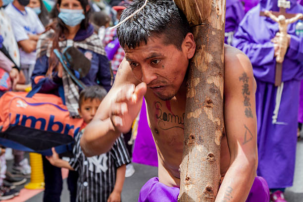 Quito, Pichincha, Ecuador - April 15, 2022: Shirtless penitent, carrying the cross as Jesus carried it on his Stations of the Cross, in a form of penance in the Jesus del Gran Poder procession, in the streets of colonial Quito.