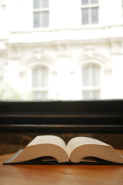 An open book is resting on a table that is situated next to a window providing soft natural light
