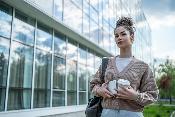 istock Confident university student holding coffee and tablet outside modern building 2207331621