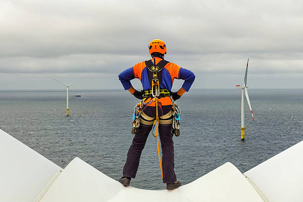 istock Rope Access Technician on Wind Turbine Hub Overlooking Sea and wind farm. 2207332129