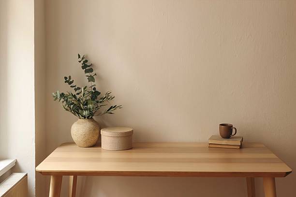 istock Textured clay vase with olive eucalyptus tree branches. Old books, round gift box. Home office table at window. Cup of tea, coffee. Minimal Scandi interior. Beige wall mockup background, copy space. 2207332596