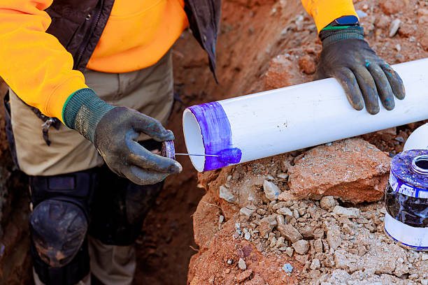 istock Worker applies purple primer to PVC pipe in construction site during daylight hours in a trench 2207333477