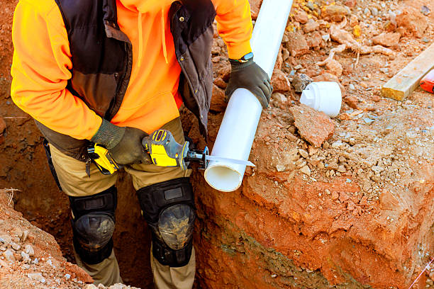 istock Worker cutting a white pipe during construction in a trench at a job site on a sunny day 2207333494