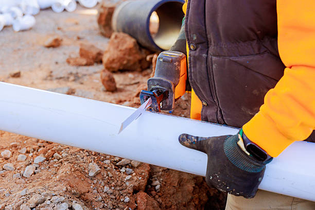 istock Worker cuts a pipe on a construction site while wearing gloves and a bright orange jacket during daytime 2207333499