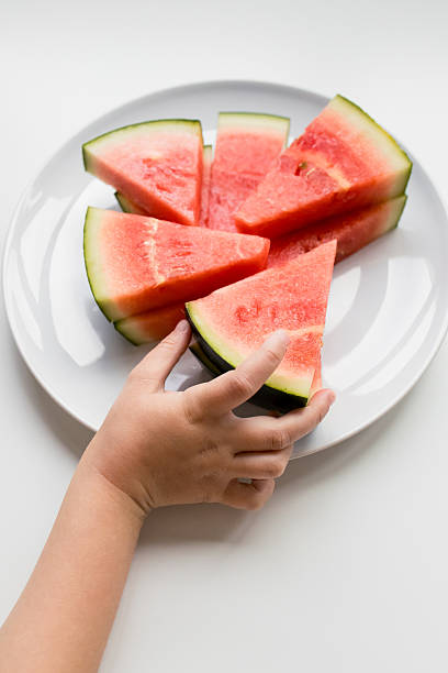 istock Child hand reaching for fresh watermelon slices on white plate 2207340770
