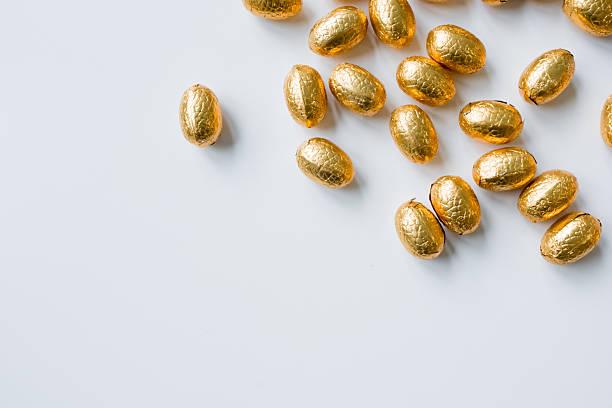 Shiny gold foil wrapped chocolate eggs on white background.