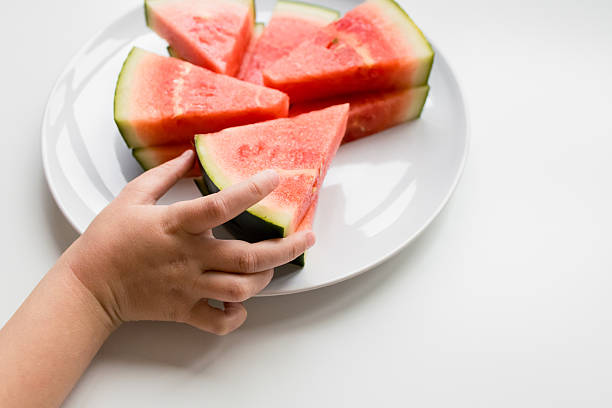 istock Child hand reaching for fresh watermelon slices on white plate 2207341301