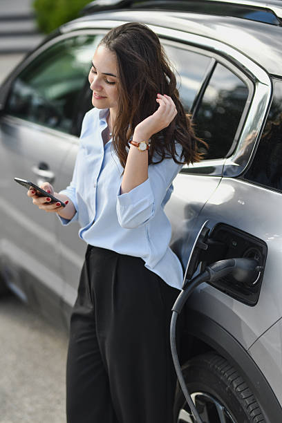 istock Smiling Woman Charging Her EV Leaning on the Car and Using Smartphone 2207353420