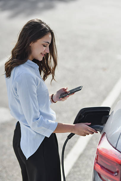 istock Happy Female Charging EV Outdoors Checking Her Phone at the Charging Station 2207353587