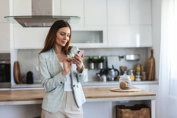 istock Smiling well dressed businesswoman text messaging while working at home office. Smiling businesswoman holding smartphone types message in corporate app reads working news in home office. 2207353897