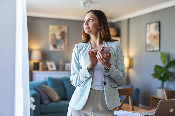 istock Smiling well dressed businesswoman text messaging while working at home office. Smiling businesswoman holding smartphone types message in corporate app reads working news in home office. 2207353898