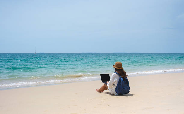 istock A female traveler using and working on laptop computer while sitting on the beach 2207355570