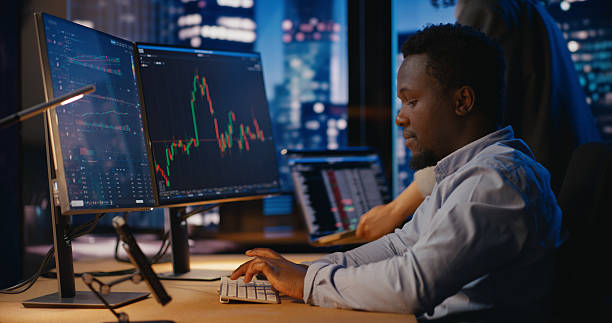istock Financial advisor works on computer in front of computer displaying live stock market charts 2207359428