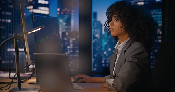 istock Female equity analyst working in the late night analyzing stock market 2207359440