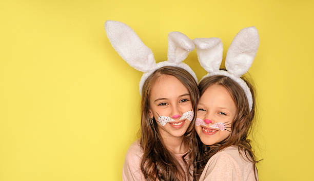 istock Funny girls in Easter bunny costumes hugging on a bright yellow studio background.  Holy Easter Day 2207361234