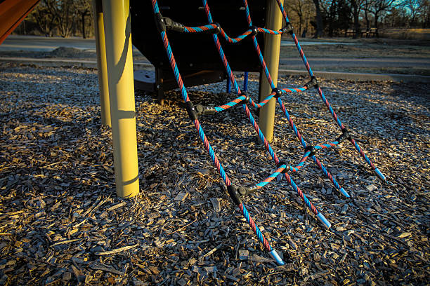 close-up of a rope climbing ladder structure on a playground covered in mulch wood chips background