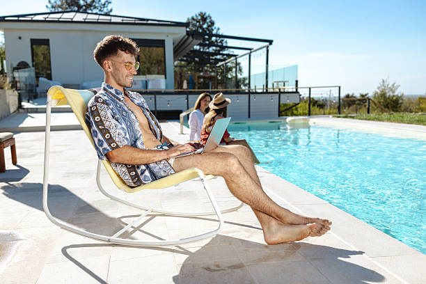 istock Man relaxing by poolside working on laptop on a sunny day 2207364548