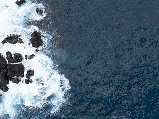 Top view with a drone filming ocean waves during low tide crashing on a rocky beach with black volcanic cliffs in southern Tenerife, wallpaper background concept