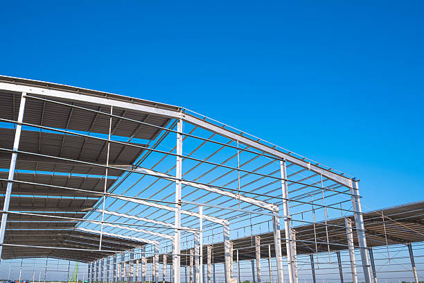 istock Factory warehouse industry building structure during install corrugated steel roofing work in construction site against blue sky background 2207367323