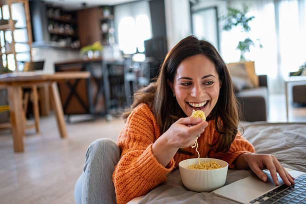 istock Young woman enjoying noodles while working from home 2207367649
