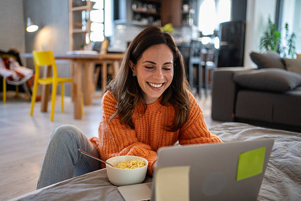 istock Young woman working from home and eating noodles while looking at laptop 2207367728