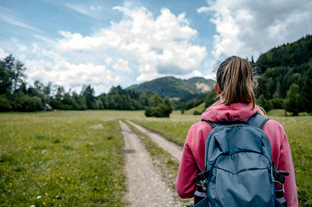 Young female hiker with a backpack standing on a gravel country road in beautiful green nature gazing into the future.