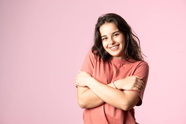 Portrait of a cheerful young woman hugging herself and smiling, isolated on a vibrant pink background