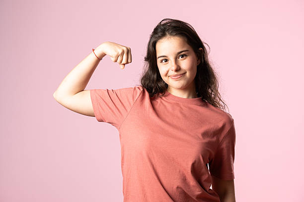 Portrait of a cheerful young woman flexing her biceps on a pink background, embodying strength and confidence