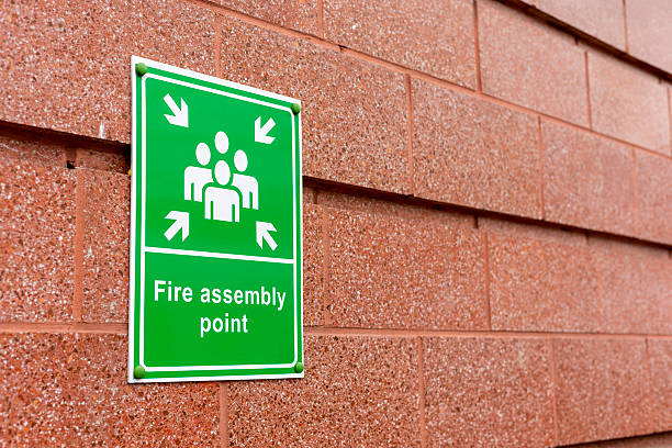istock Green and White Fire Assembly Point Sign on a Modern Brick Wall Building for Emergency Evacuation Point 2207381171
