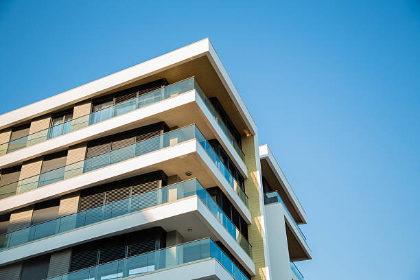 A close-up of a contemporary residential building featuring sleek white balconies, large windows, and stylish black metal shades. The elegant contrast of materials and minimalist design make this image perfect for themes related to architecture, real estate, construction, apartment rentals, and urban living.