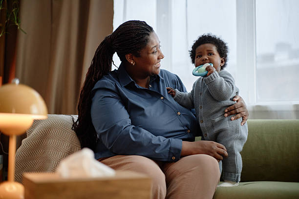istock Smiling Black Woman Hugging Happy Baby Girl Biting Teether on Couch 2207387891