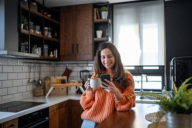 istock Smiling woman enjoying morning coffee and using smartphone in modern kitchen 2207396099