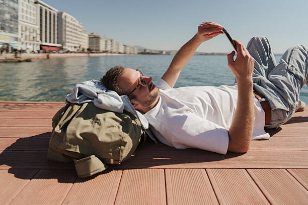 Photo of a man enjoying springtime sun on the pier and using his smartphone