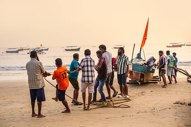 Fishermen aboard a traditional wooden boat near the Kerala - India shoreline prepare for or return from a fishing trip. The curved vessel, shallow waves, and open sea backdrop capture a moment of coastal livelihood and maritime heritage.