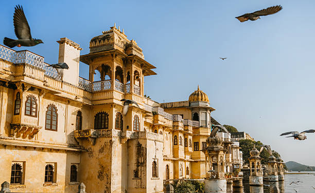 Golden hour photograph of an ornate heritage building with flying birds in Udaipur, India, presenting intricate traditional artistry and serene cultural charm along the waterfront.