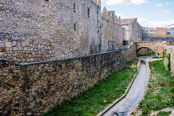 istock Historic stone wall and bridge alongside a tranquil waterway in Sant Mateu, Castellon, Valencia under a bright blue sky 2207409787