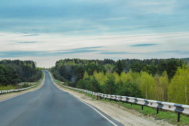 A smooth asphalt road with white lane markings curves gently through rolling green countryside under a magnificent sky filled with puffy white and gray clouds. The scene represents liberation and potential, symbolizing the freedom to choose one's direction and the optimism found in open spaces and endless horizons.