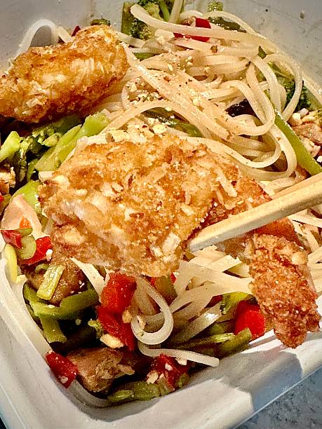 Bowl of rice noodles, chicken and shrimp with peppers and bean sprouts and peanuts.