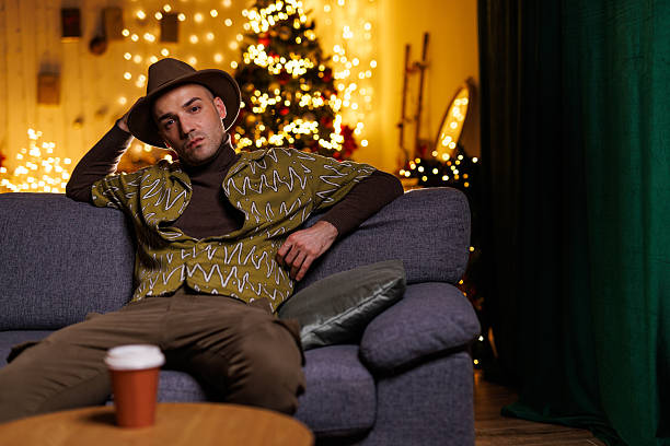 istock Man relaxing on sofa with festive lights and a Christmas tree in background 2207411782