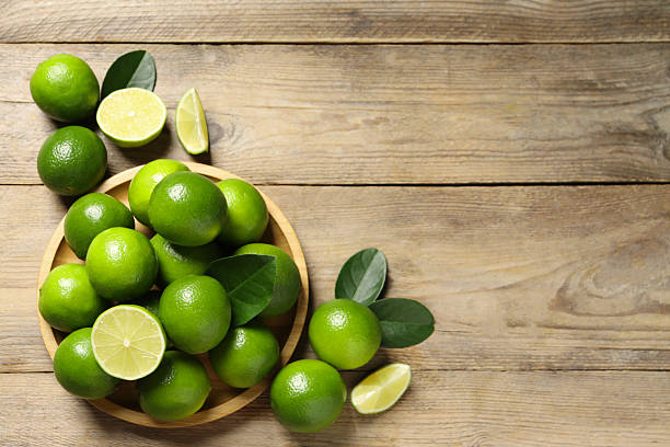 istock Fresh limes and green leaves on wooden table, flat lay. Space for text 2207413436