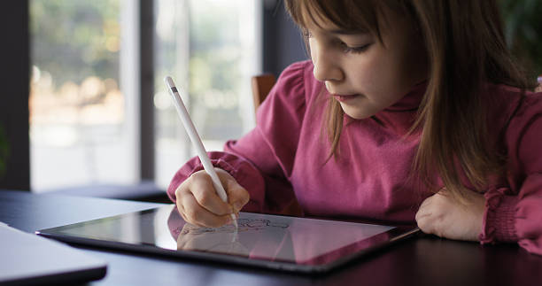 istock Child girl watching online tutorial on laptop computer and drawing digital pictures using digitized pen and digital tablet 2207436679