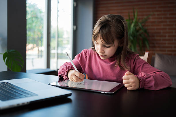istock Child girl watching online tutorial on laptop computer and drawing digital pictures using digitized pen and digital tablet 2207436713