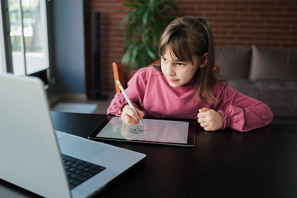 istock Child girl watching online tutorial on laptop computer and drawing digital pictures using digitized pen and digital tablet 2207436759